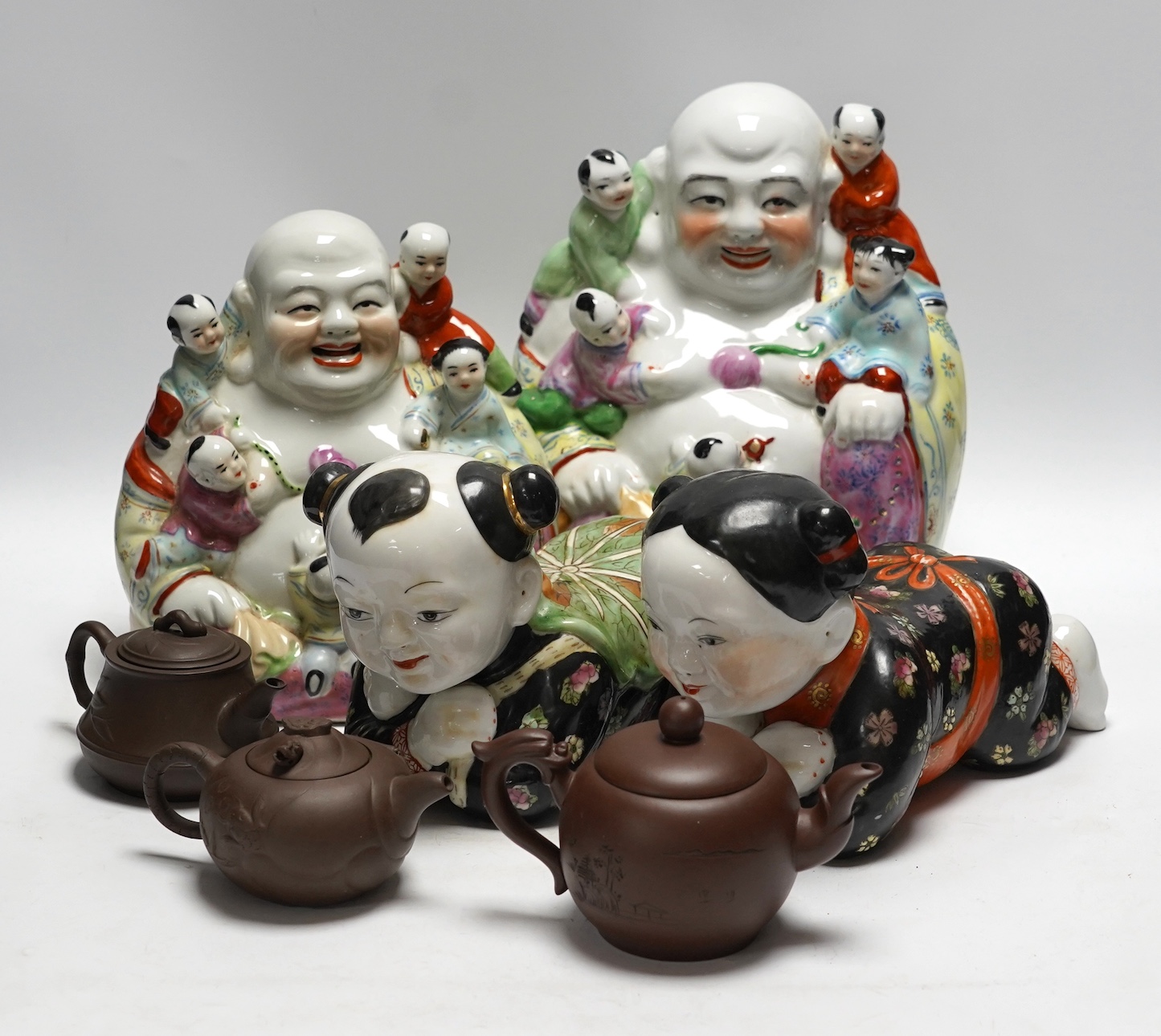 Two figural Chinese pillows, two famille rose Budai groups and three yixing teapots, tallest 25cm